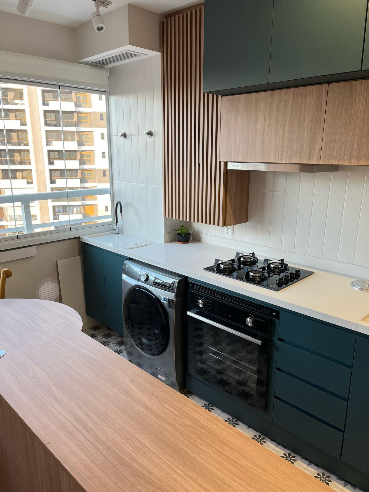 Cozinha planejada com armários em tons de cinza e branco, bancada de mármore e eletrodomésticos embutidos, criando um ambiente funcional e elegante.