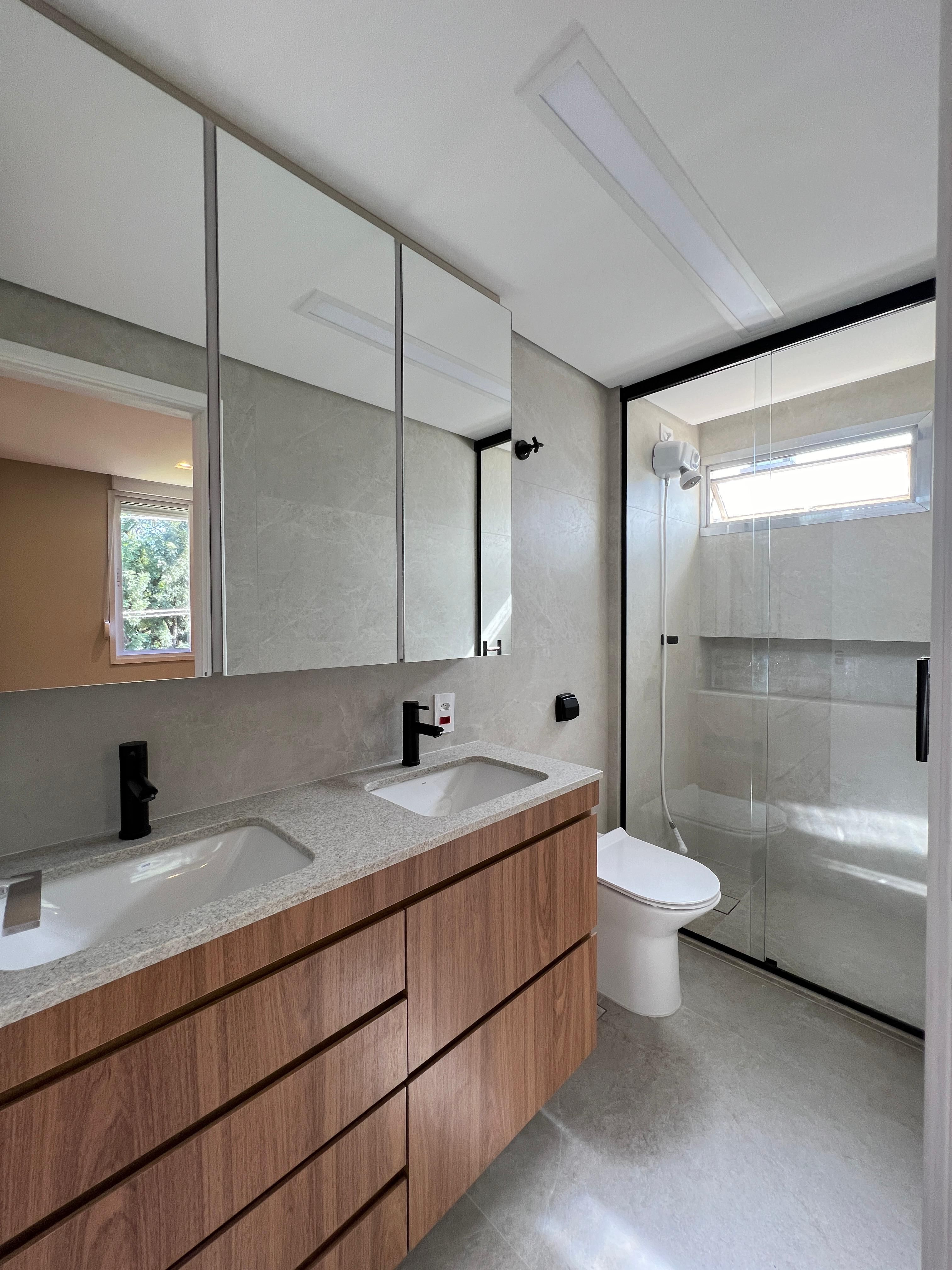 Banheiro planejado com armários madeira escura, pia de mármore e espelho grande.