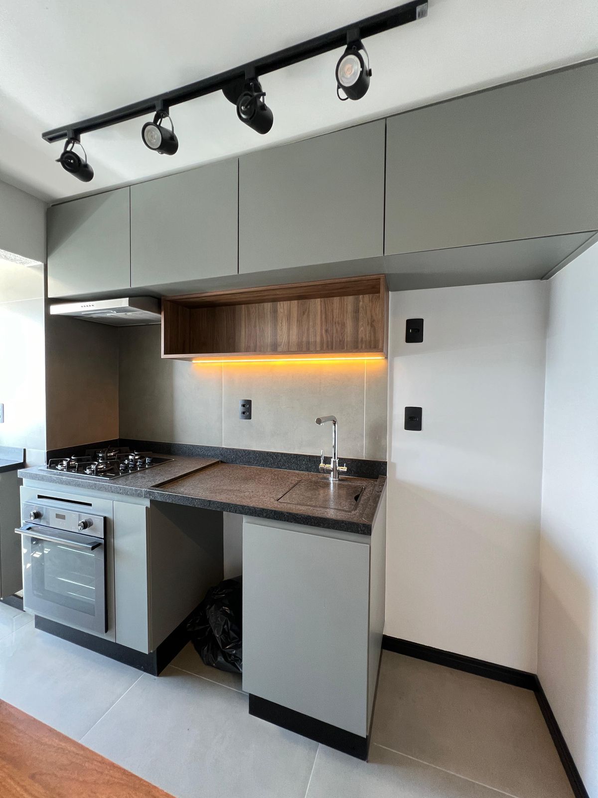 Cozinha clean com armários brancos sem puxadores, bancada clara e piso de porcelanato, transmitindo leveza e amplitude.