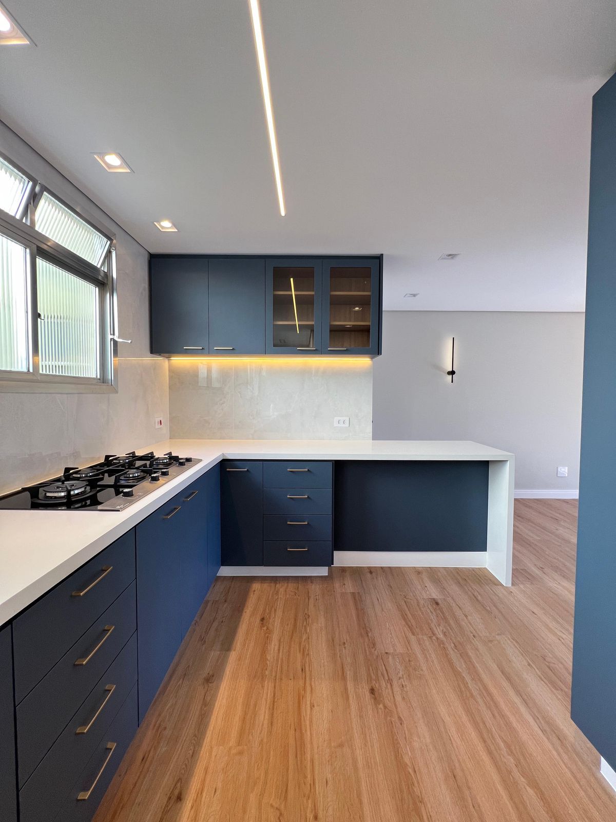 Cozinha gourmet integrada à sala, com armários em tons neutros, torre de fornos e uma ampla bancada para refeições.