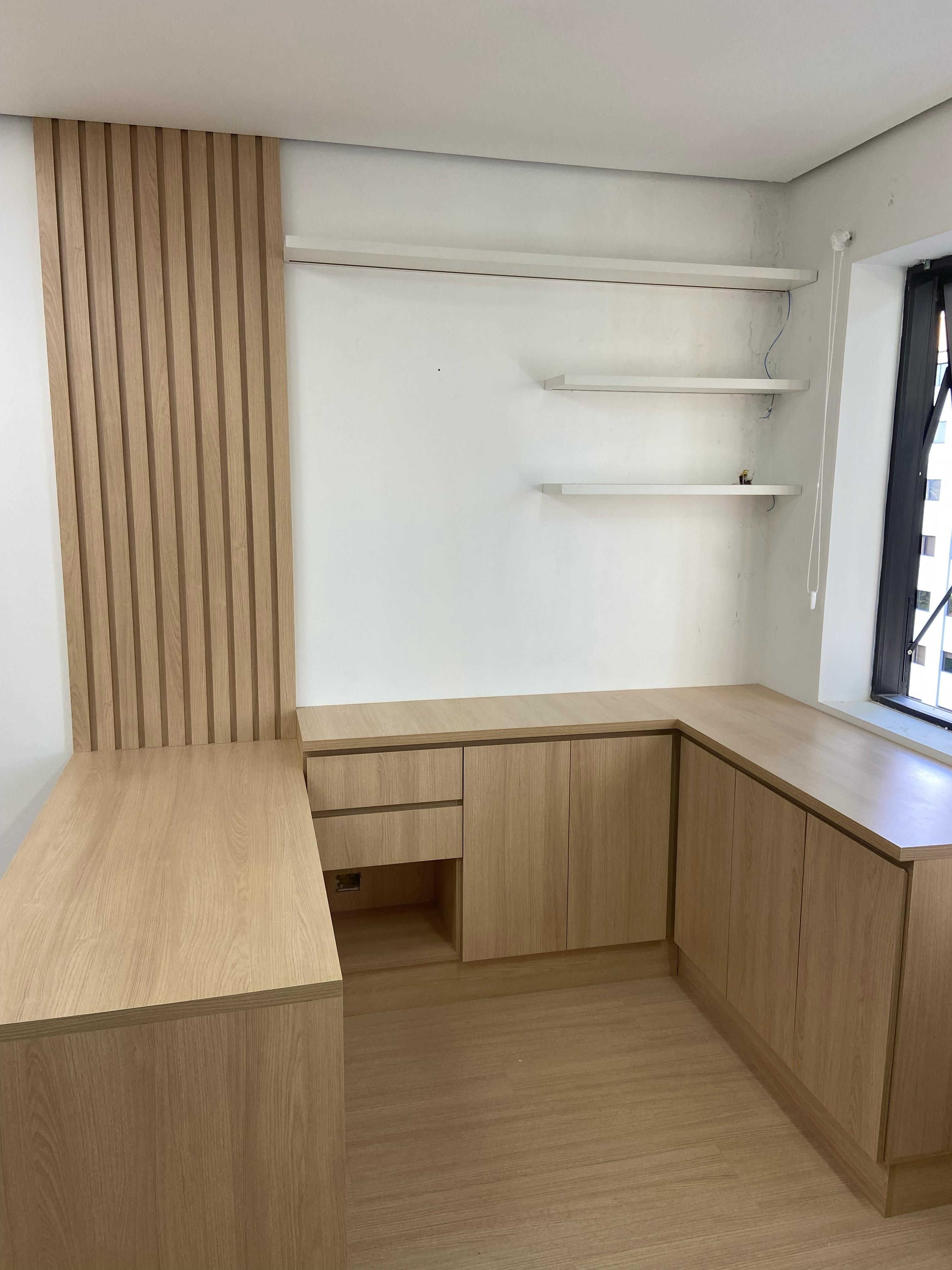 Escritório planejado com móveis de madeira clara, cadeira preta e decoração moderna.